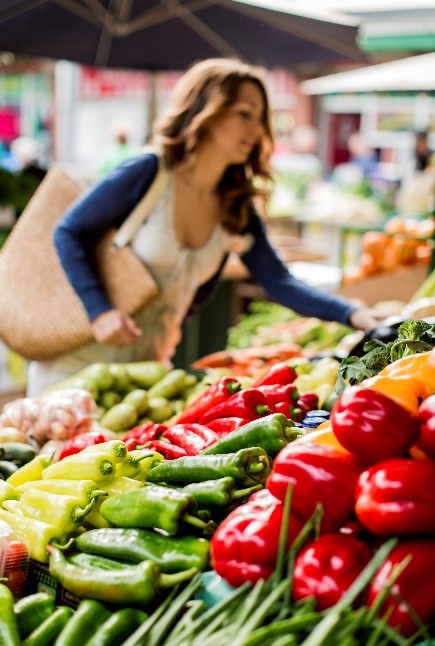 Image focused on vegetables, a woman browsing vegetables in the background